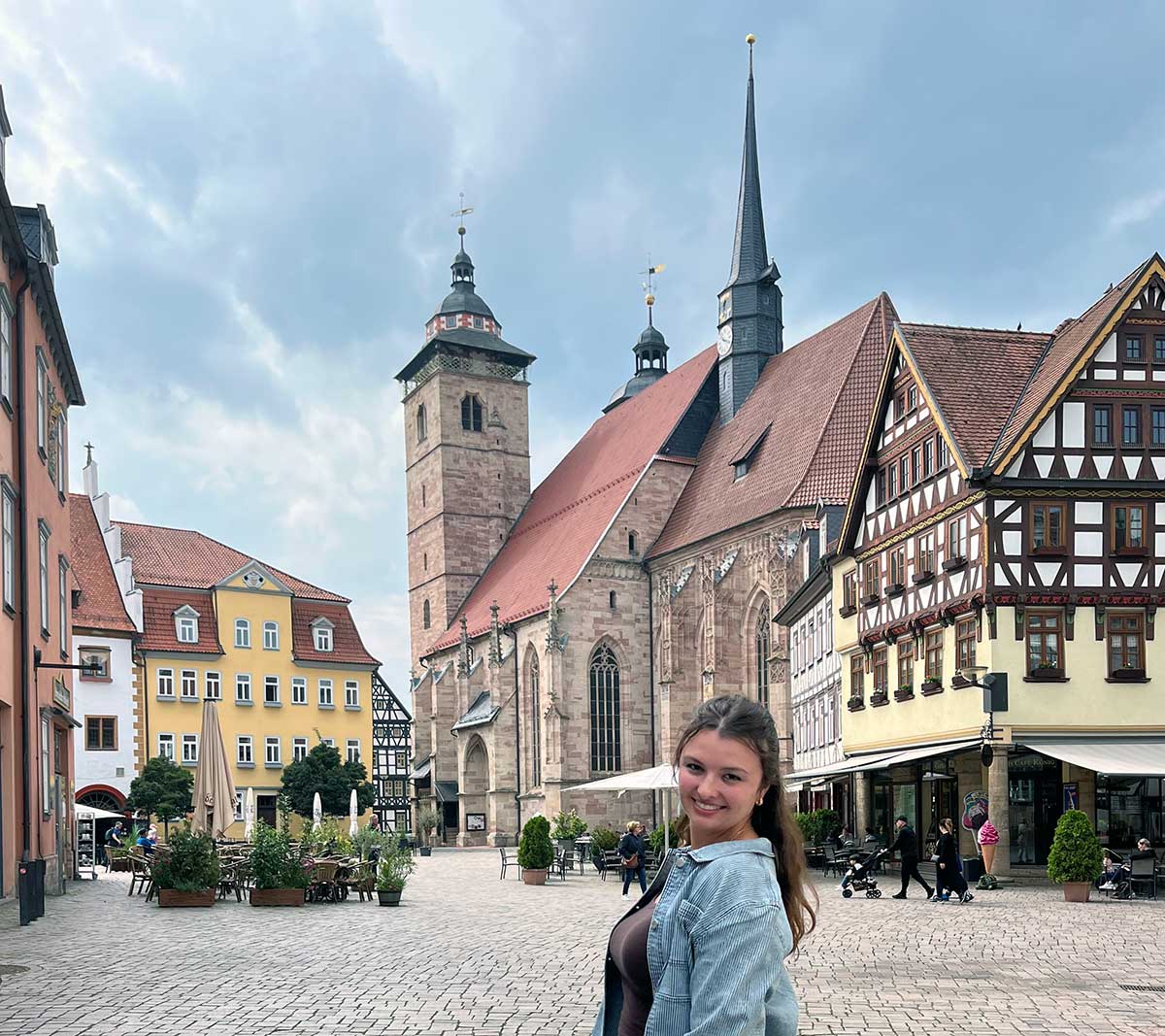 Person standing in a historic European town square with timber‑frame buildings and a large church.