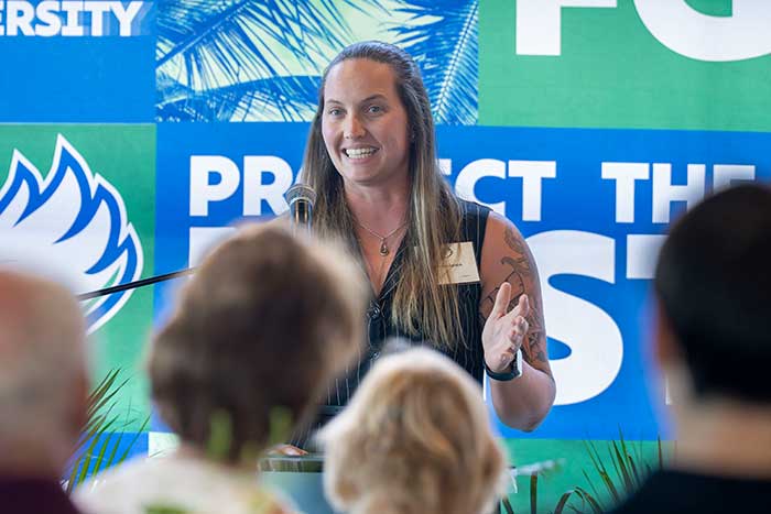 Event speaker stands at podium addressing audience, with FGCU branding displayed behind.