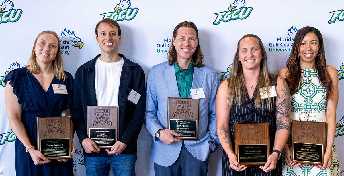 Five FGCU Athletics Hall of Fame inductees hold plaques before FGCU logo backdrop.
