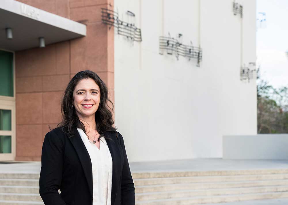 Person standing outside FGCU building with metal music notes on wall.