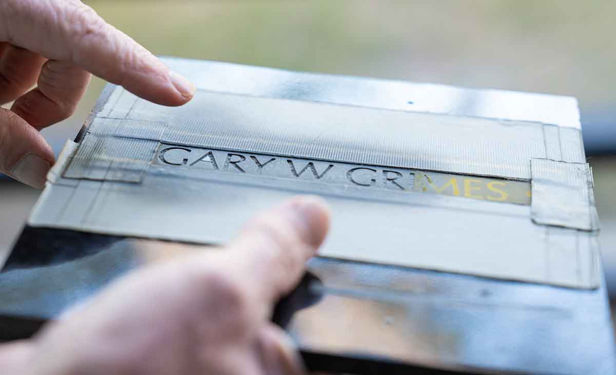 A close-up of a name carved in all capital letters in a square of granite. The name reads Gary W Grimes