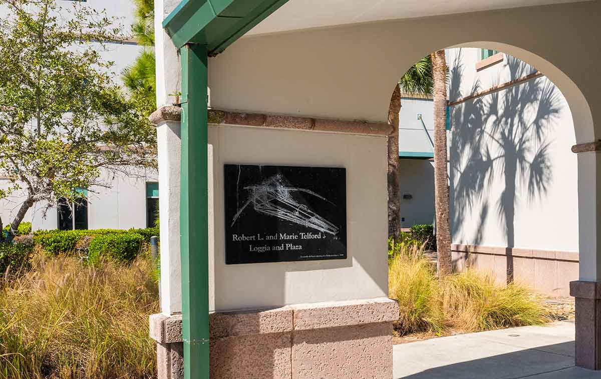 An outdoor photo of a wall with a black granite etching of a flying machine