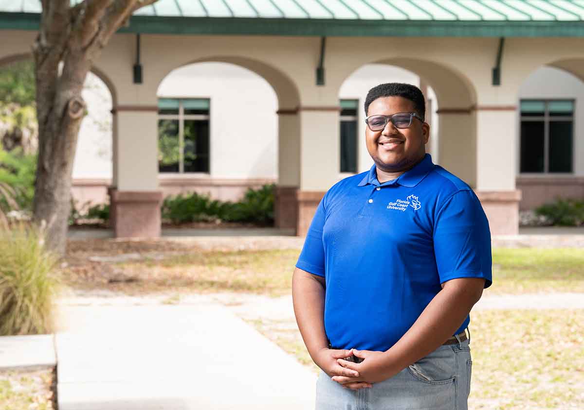 A smiling man in glasses and a blue polo shirt with the FGCU logo and wordmark embroidered on it stands outdoors