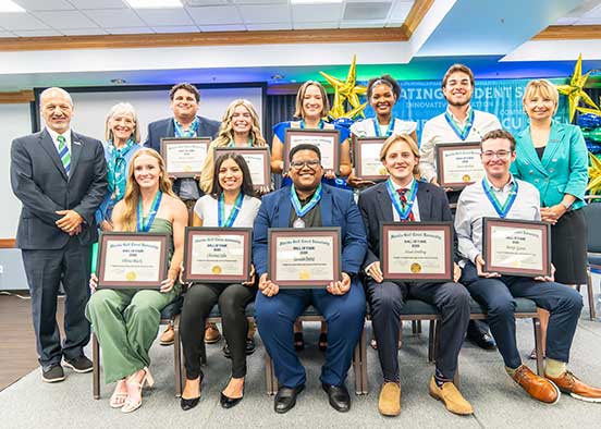 A group photo of 8 people in the back row and 5 people in the front row, with 10 total holding framed certificates that state Hall of Fame