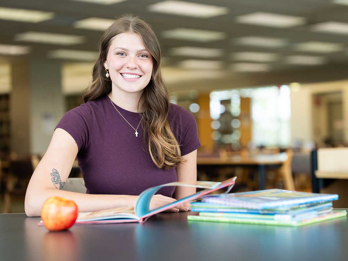 FGCU education student with textbooks and apple in campus library
