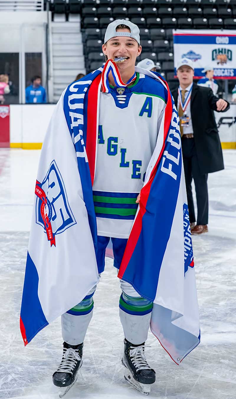 FGCU hockey player wrapped in ACHA championship banner on ice