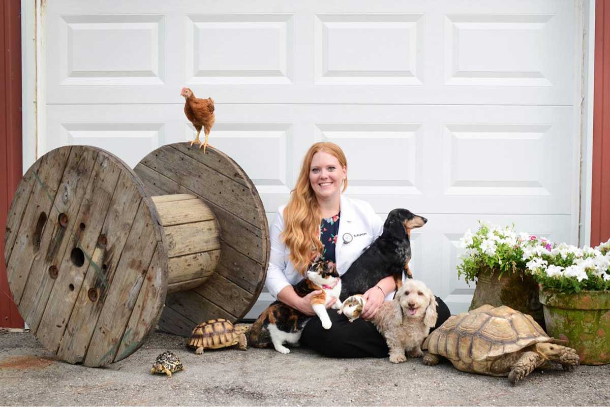 Veterinarian seated with dogs, cats, tortoises and chicken outdoors