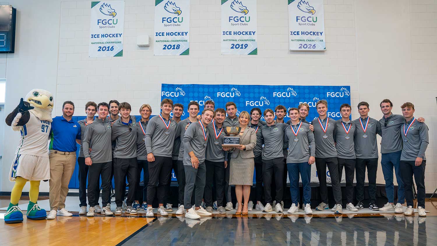 FGCU ice hockey team holds ACHA Division II championship trophy beneath banners