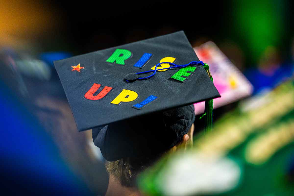 A mortarboard on someone's head reads Rise Up