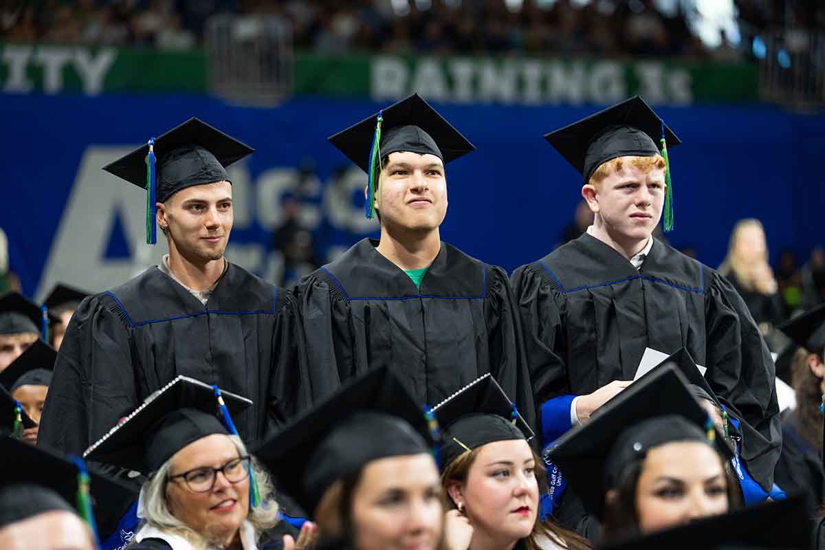 Three men in black graduation gowns and mortarboards stand during a commencement ceremony