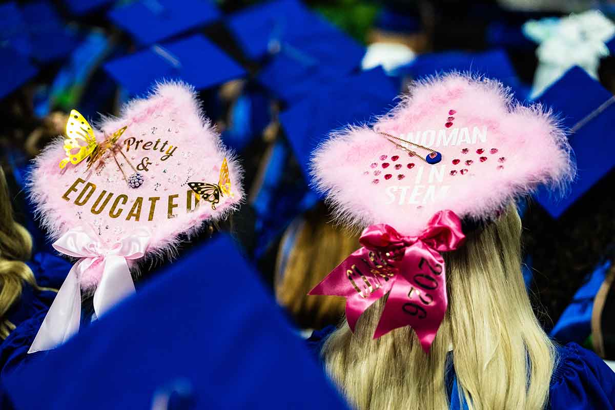 Two pink decorated mortarboards. The left one reads pretty and educated and the right one reads woman in STEM