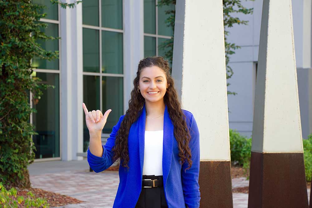 FGCU student showing Wings Up gesture on campus near academic building