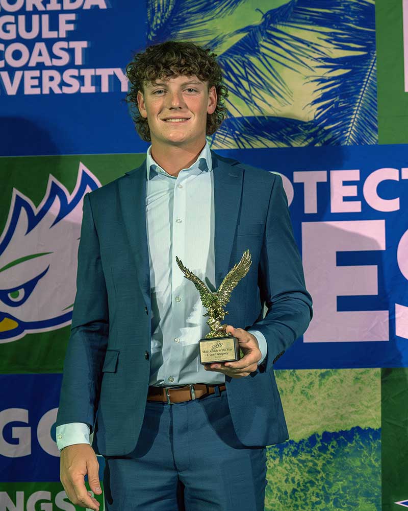 FGCU baseball player holds award at university event backdrop and logo display