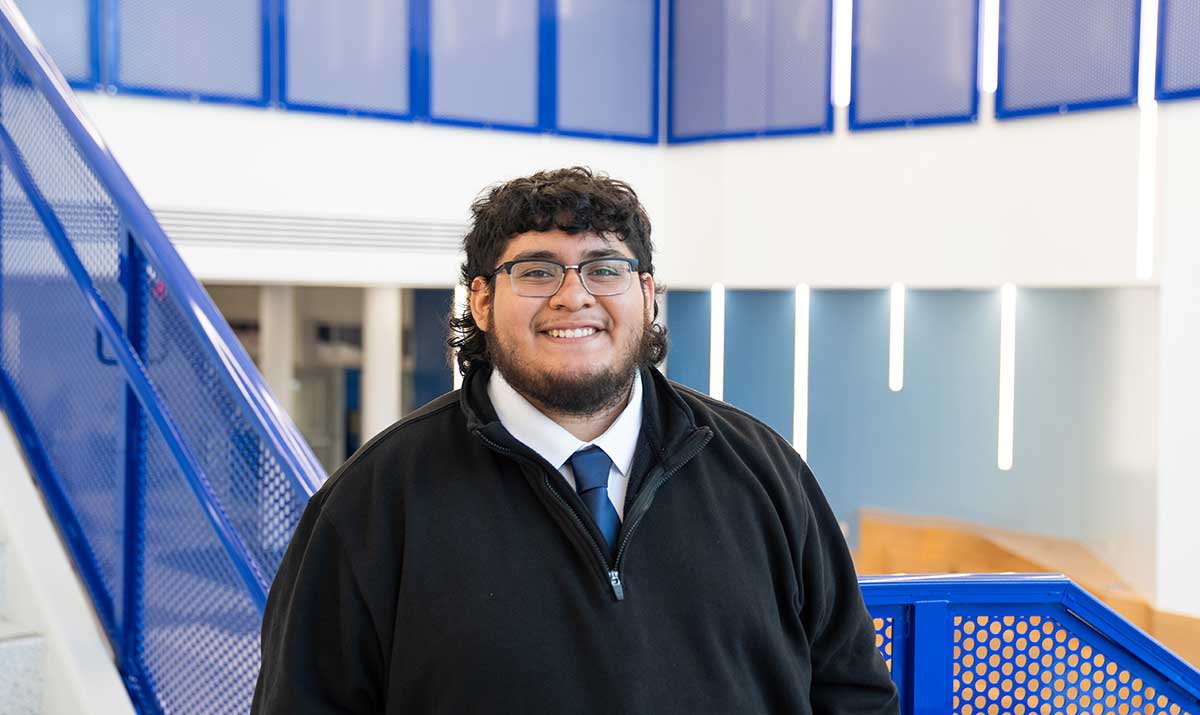 FGCU student wearing black jacket standing near blue stair rail