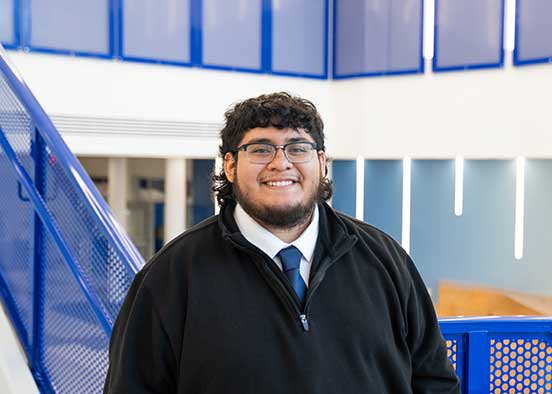FGCU student wearing black jacket standing near blue stair rail