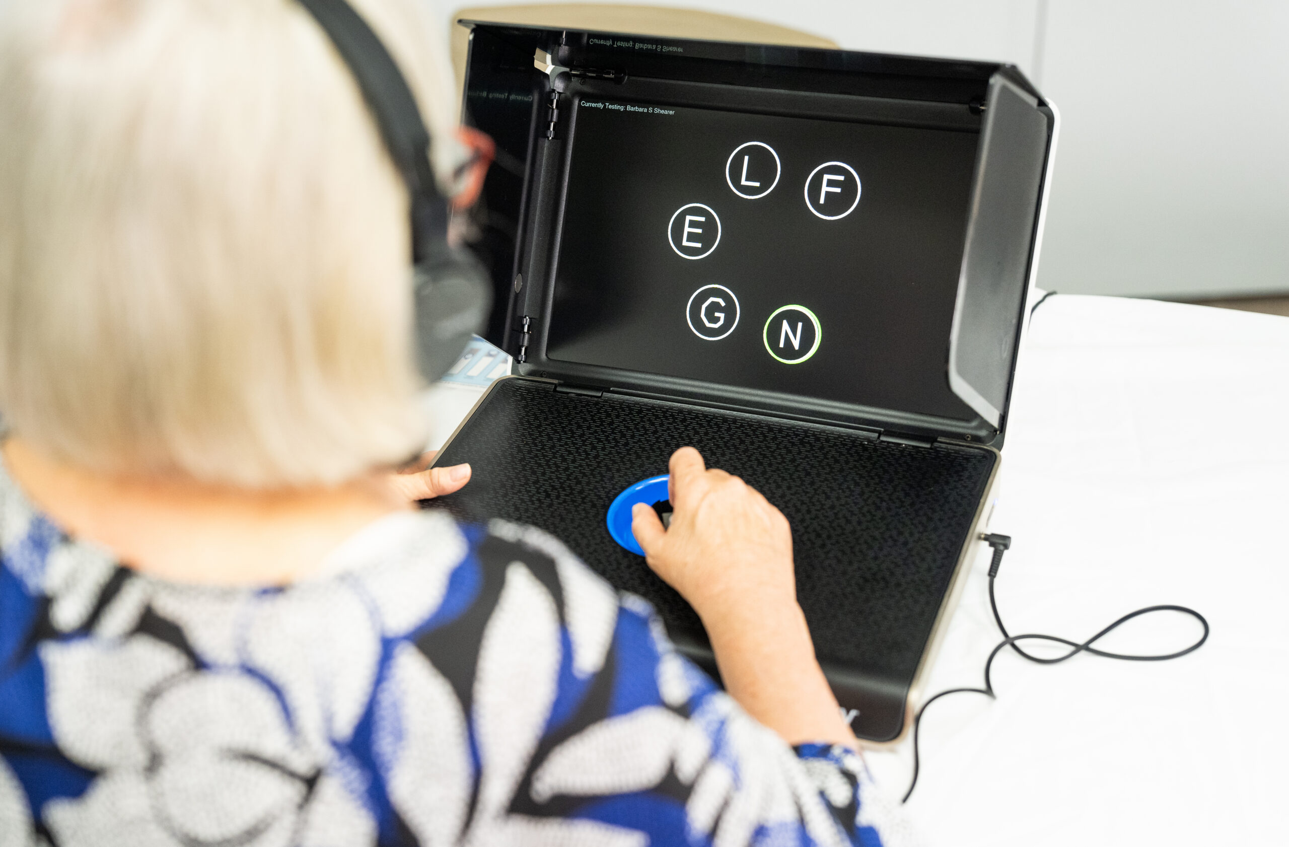 An older woman with short, blond hair, takes a computer exam with letters in circles on the screen