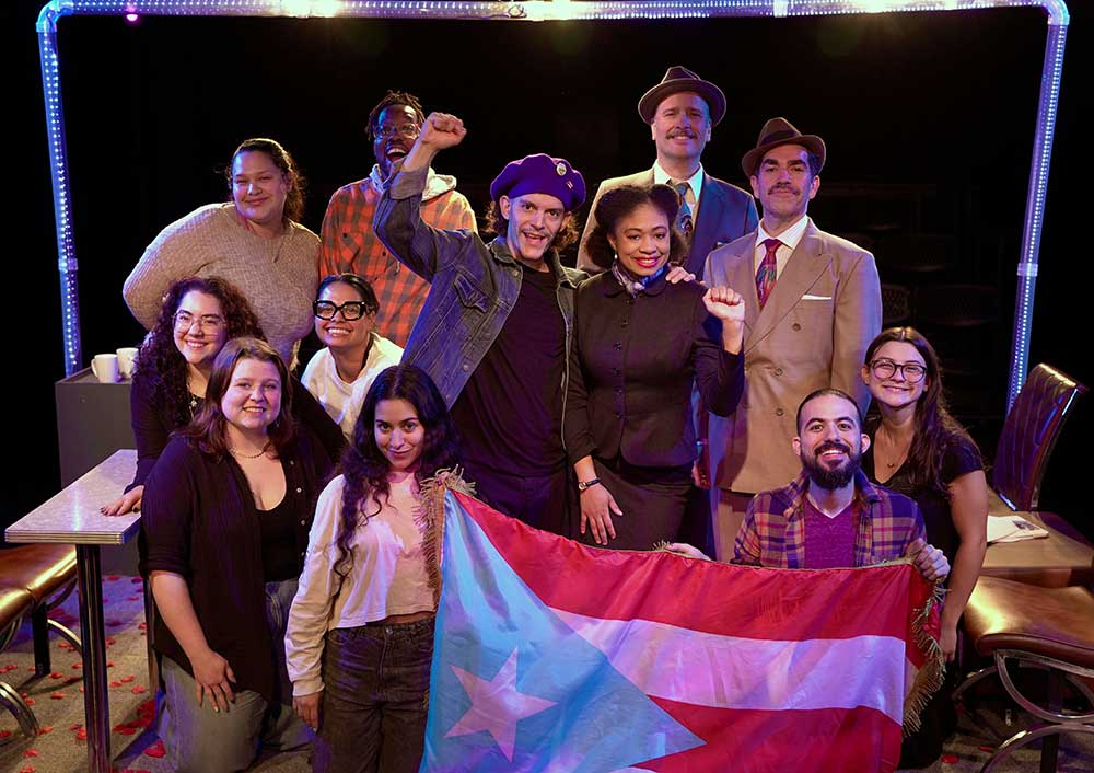 Ensemble cast on stage holding Puerto Rican flag during theater production