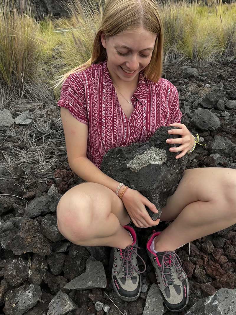 Geology student examining volcanic rock sample in lava field