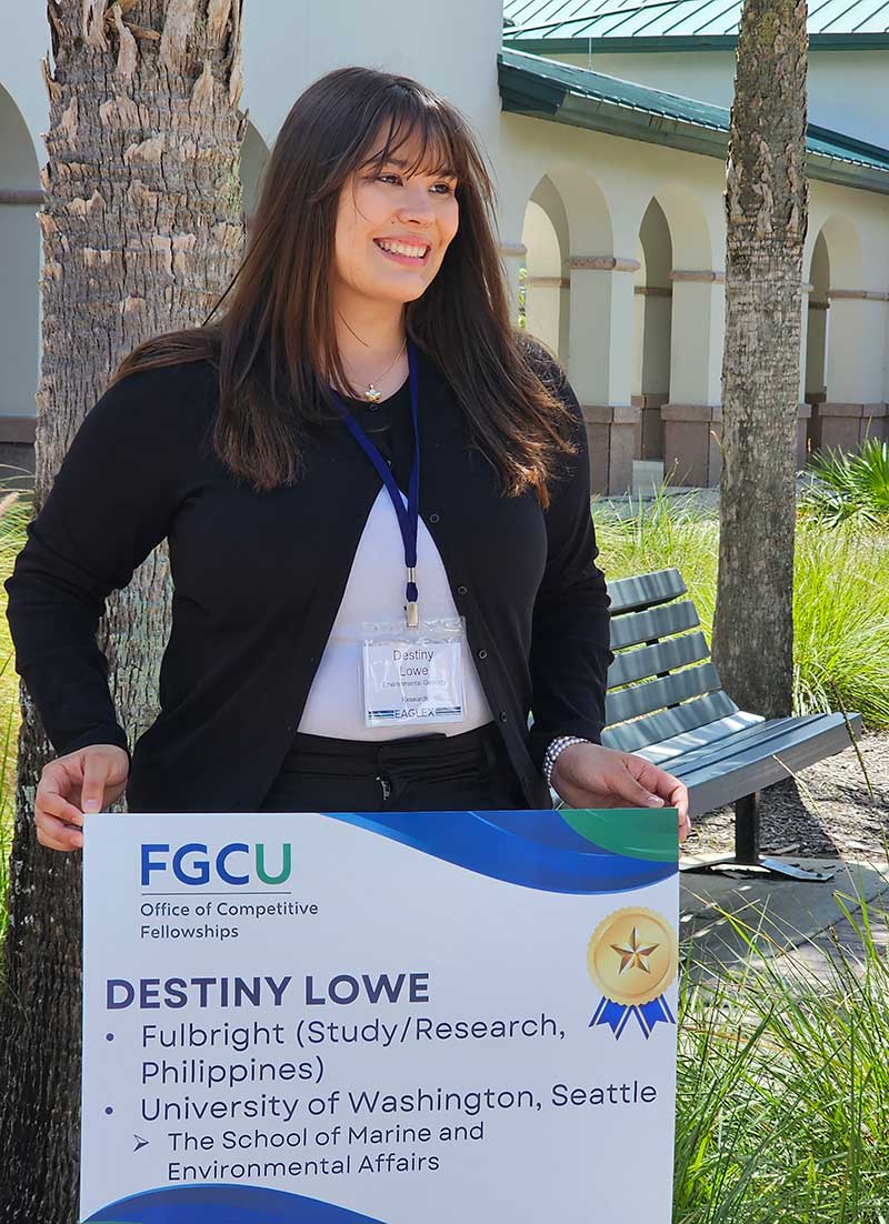 Woman standing outdoors holding a placard announcing her as a Fulbright recipient