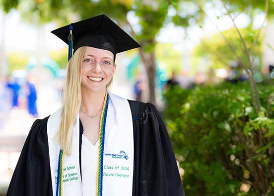 College graduate in cap and gown outdoors, Class of 2024 stole