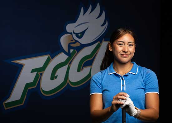 FGCU golf management student poses with club in front of FGCU logo wall