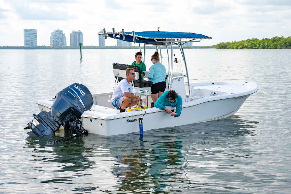 Four people on a boat with a cloudy, blue sky and large condominiums in the background