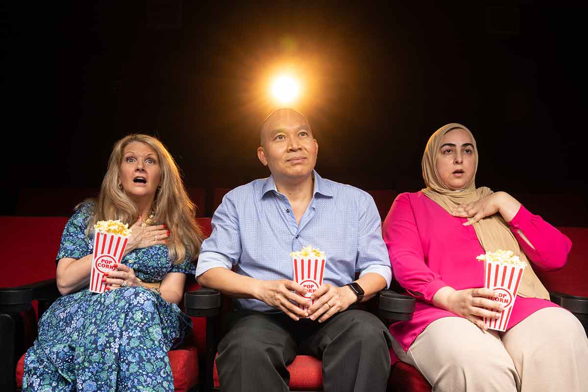 Three people sit in cinema chairs, holding popcorn containers, as if watching a movie