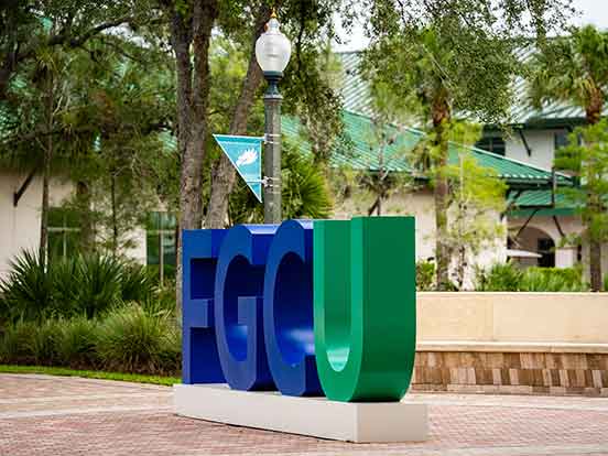 A beauty shot of the FGCU campus and a large FGCU sign, where the FGC is blue and the U is green
