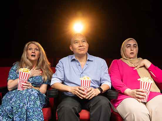 Three people sit in cinema chairs, holding popcorn containers, as if watching a movie