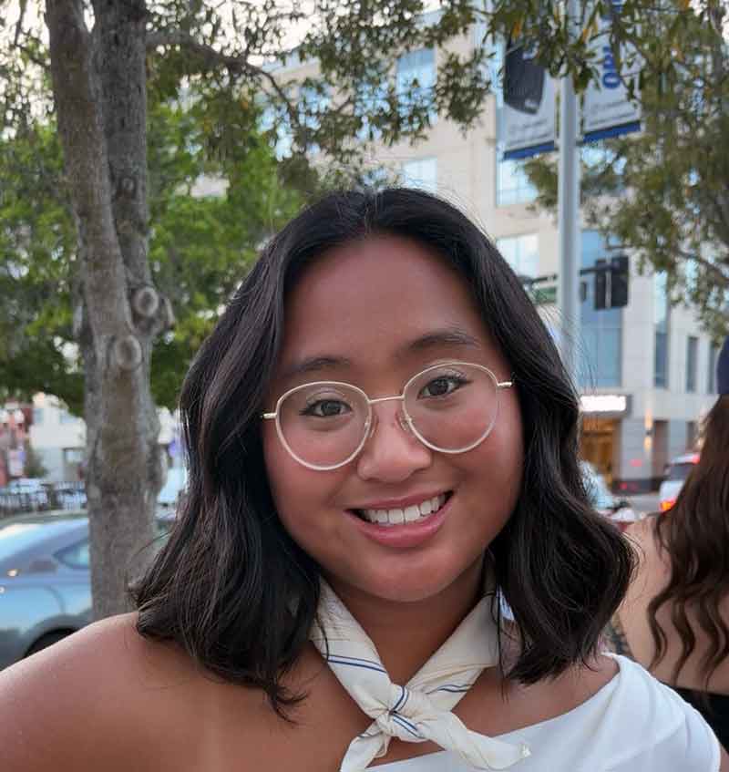 A young woman with short, brown hair and glasses stands outdoors