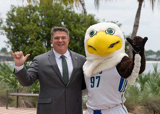 Person in gray suit standing next to FGCU’s Azul the Eagle mascot