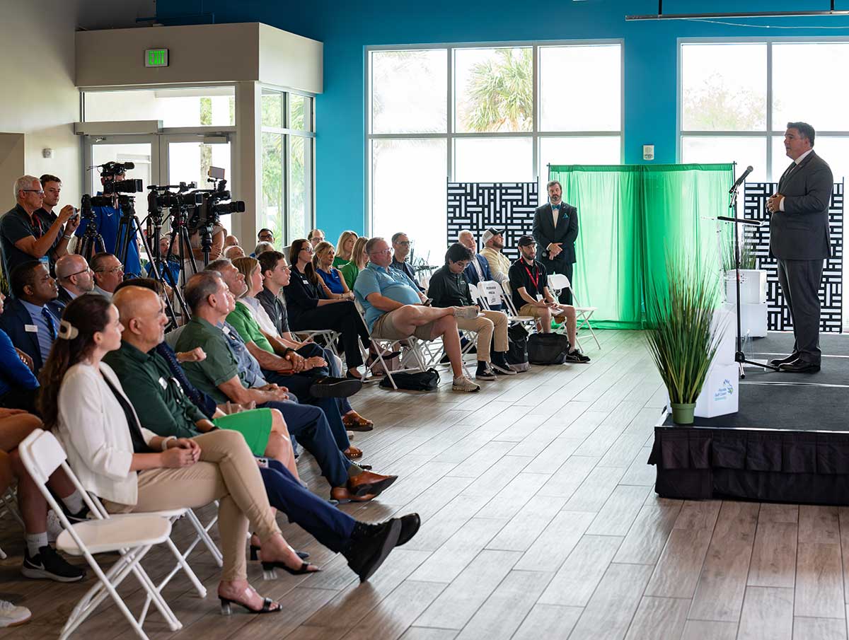 Person at podium addresses a group of people seating indoors.