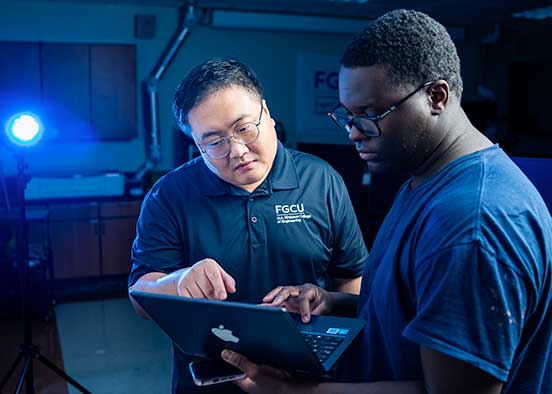 Two men standing at a computer analyze code in a research lab
