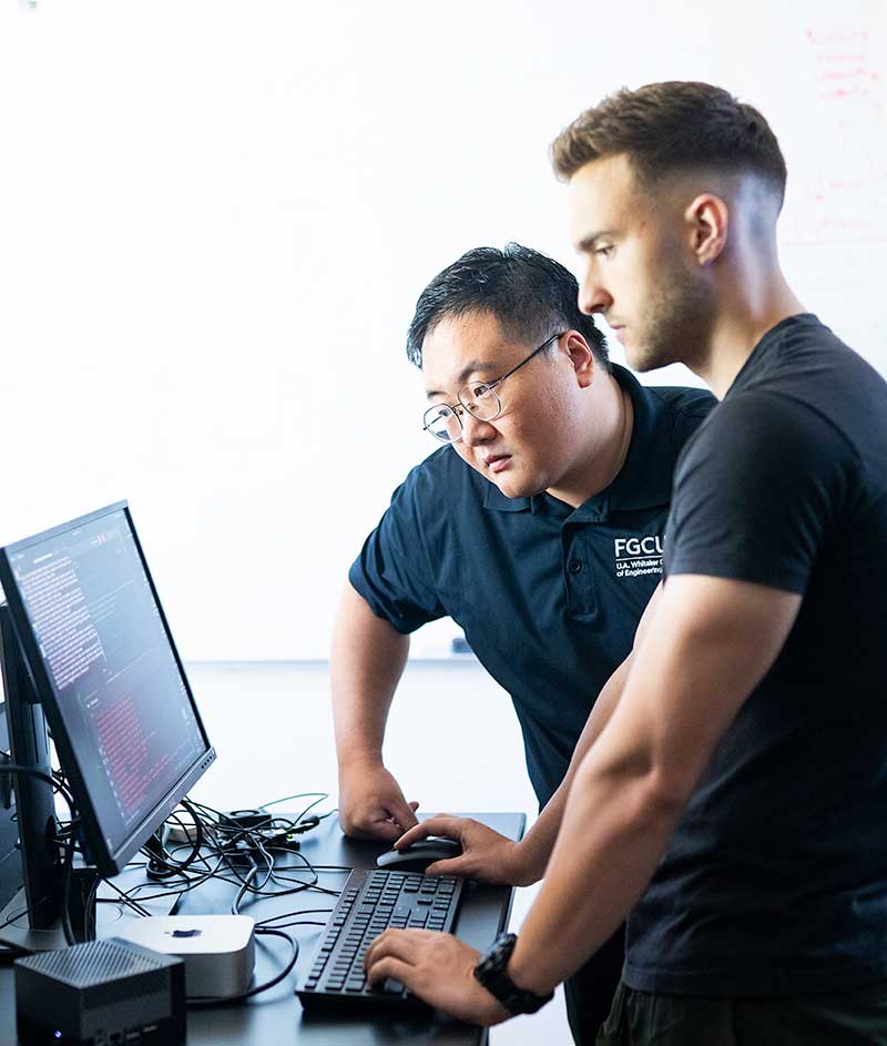 Two men standing at a computer analyze code in a research lab