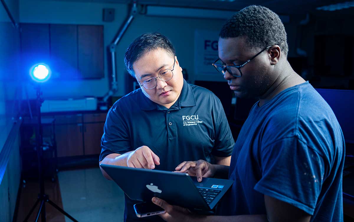 Two men standing at a computer analyze code in a research lab