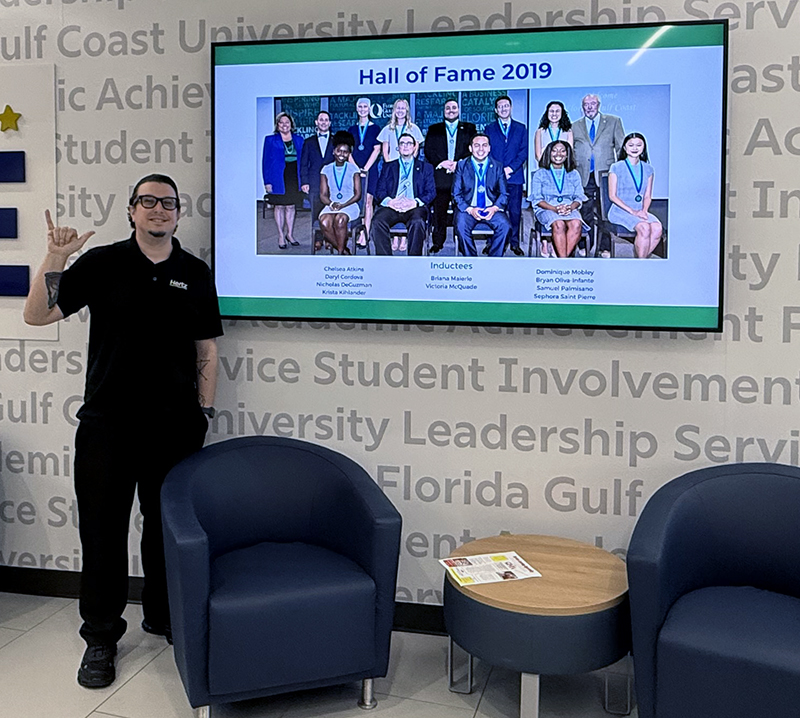 FGCU alumnus stands beside 2019 Hall of Fame display honoring student leaders