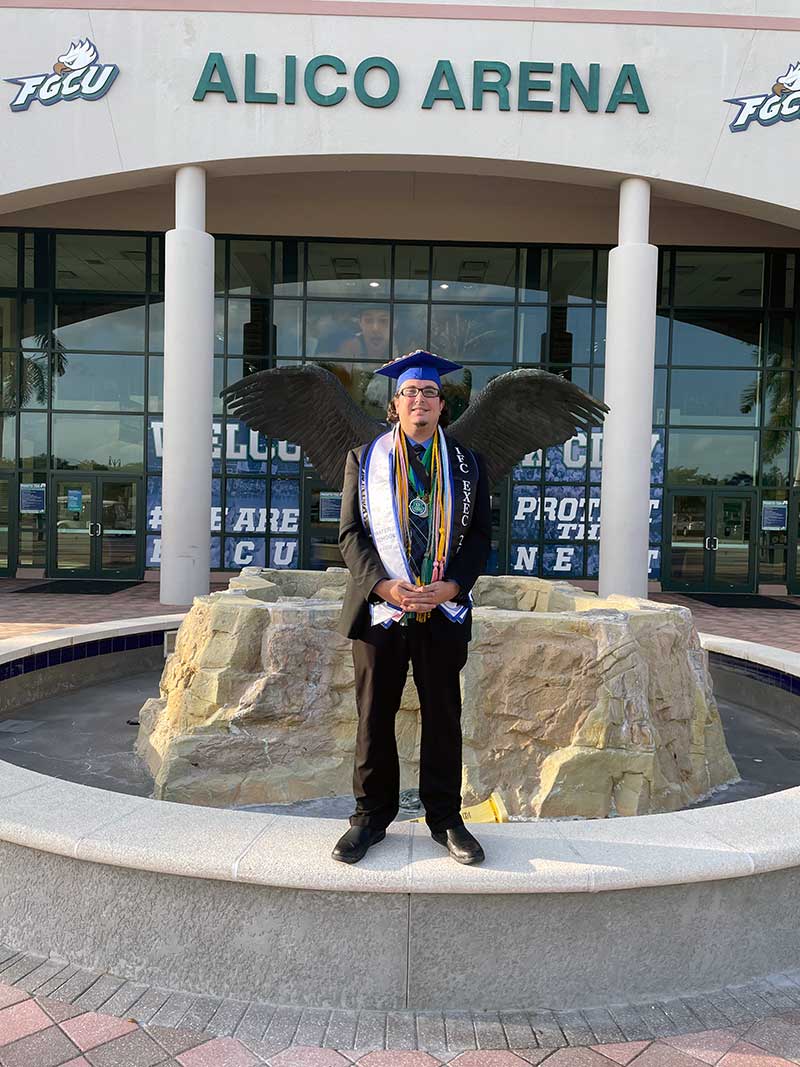 FGCU graduate stands at Eagle Fountain near Alico Arena entrance