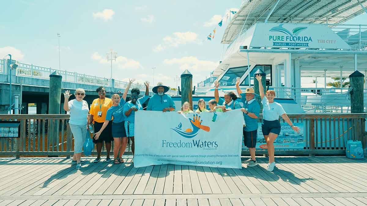 A group photo of people on a boat deck in front of a boat, with the people in the middle holding a sign that read Freedom Waters