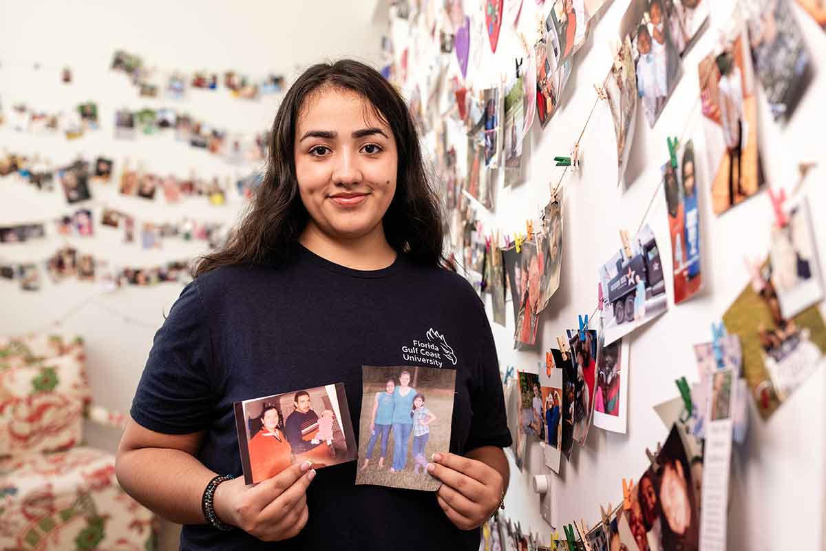 A young woman holds up two older photos before hanging them on two walls covered in photos