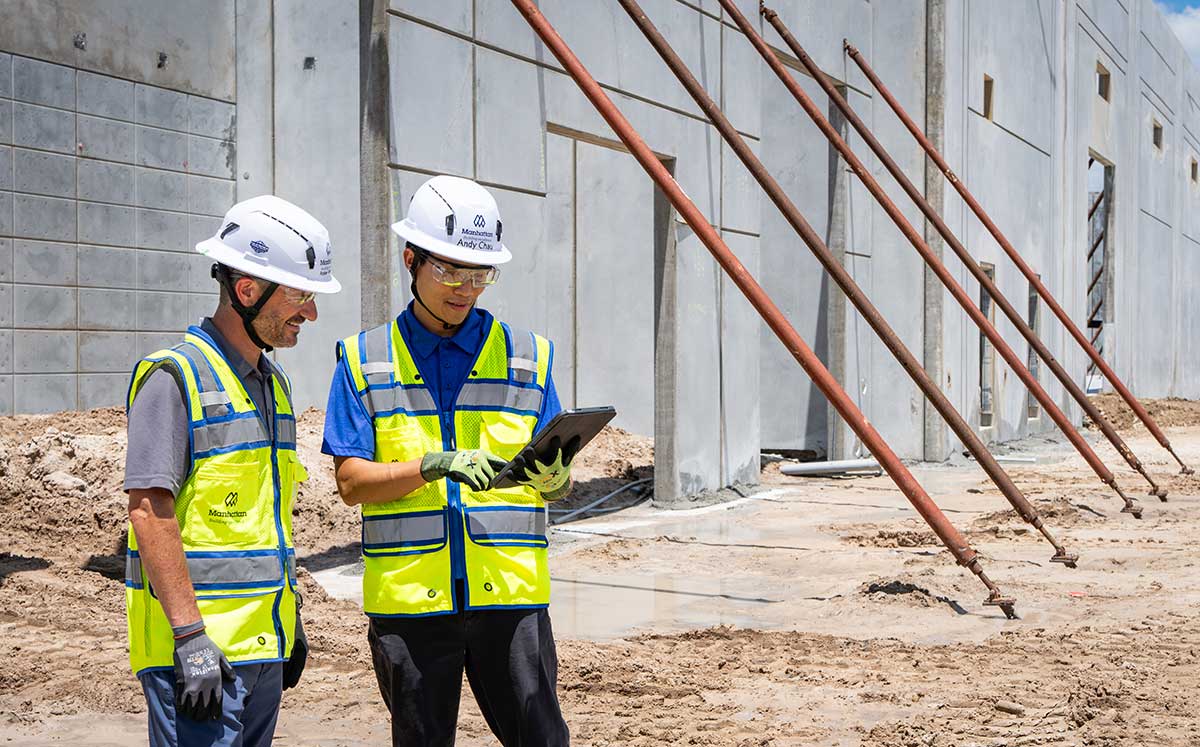 Construction managers review digital plans at concrete building site