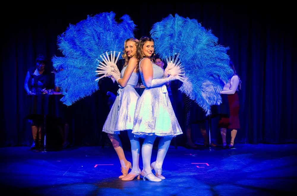 Two actors perform in musical theater production with feather fans