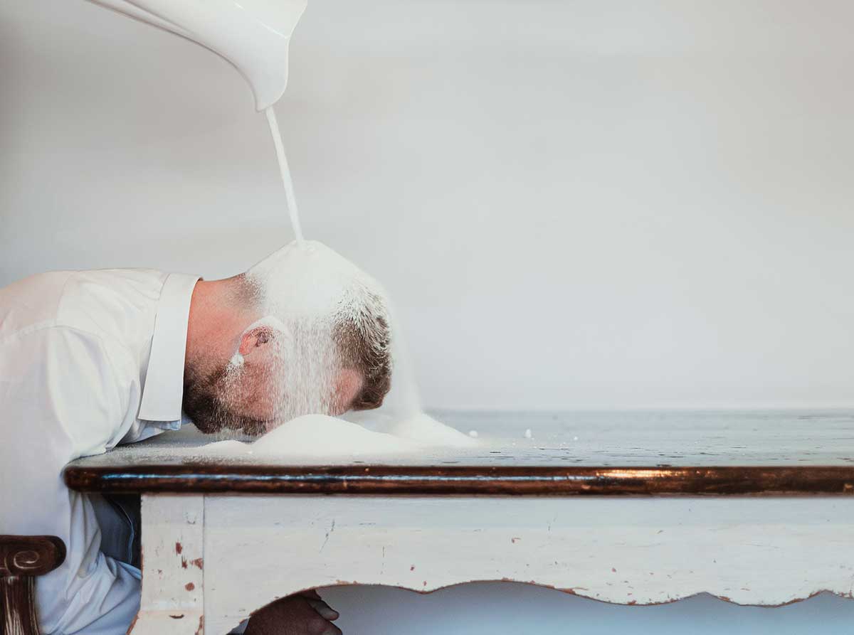 Person with head on table as white powder pours down from above