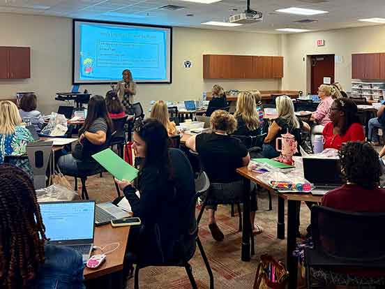 A classroom full of seated adults and an instructor at the front of the room with a presentation on a whiteboard